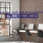 An image of a modern co-working space with a textured, multicolored reddish-brown wall. There is a long wooden desk with four computers and chairs in front of the wall. The text "Transform Your Walls with Multicolored Elegance" and "LUXTURE STONE FINISH" is overlaid on the image.