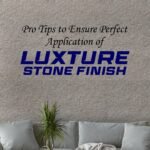An image of a living room with a gray sofa and potted plants in front of a wall with a finely textured, beige stone finish. The text "Pro Tips to Ensure Perfect Application of LUXTURE STONE FINISH" is written on the wall.